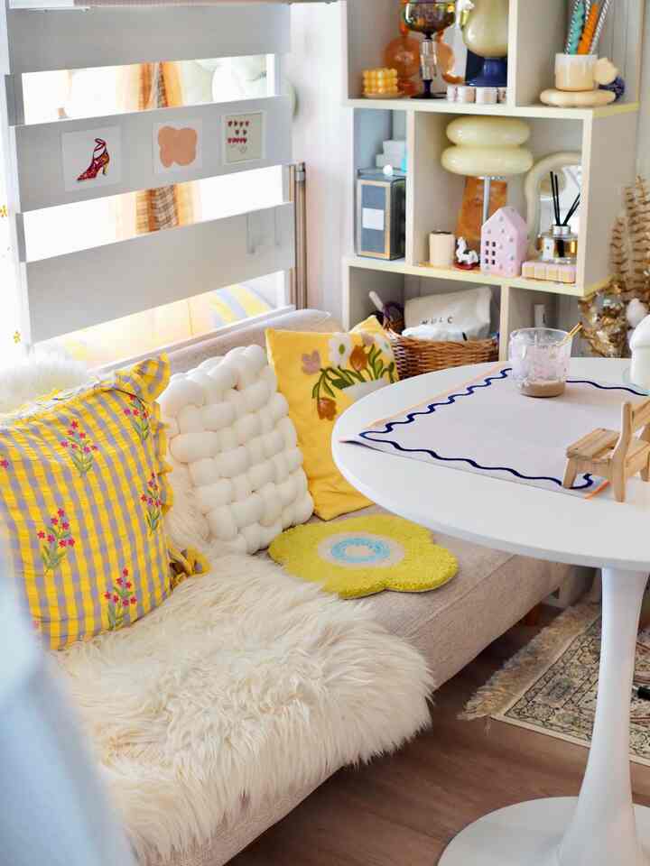 明るいホワイトとイエローのトーンのリビング、居心地の良いクッションとホワイトの丸テーブルが配置された自然な雰囲気のインテリア