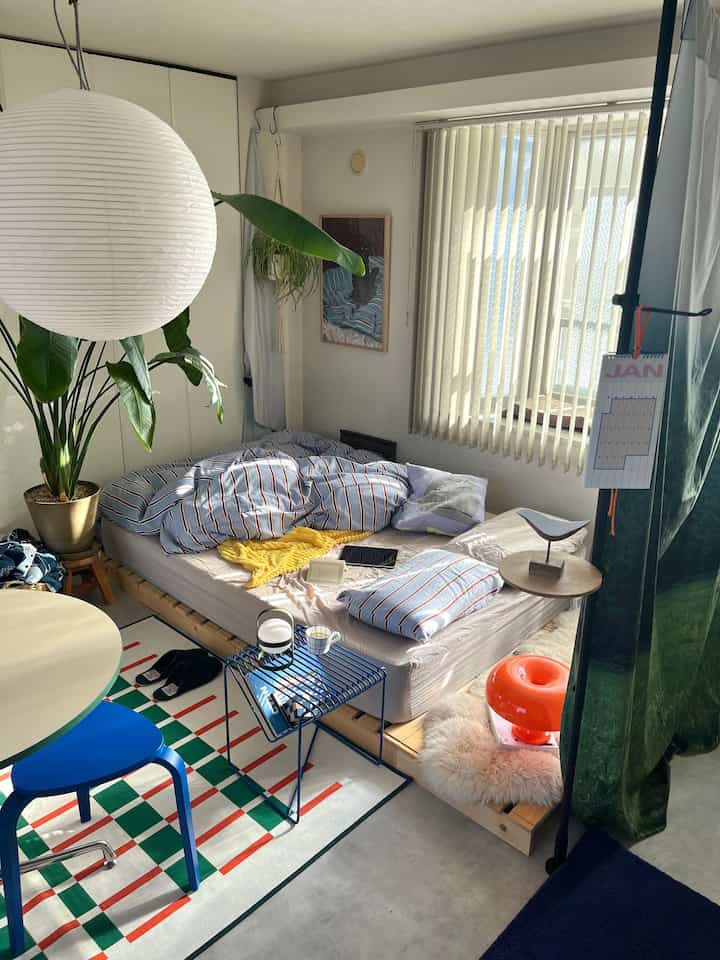 白を基調とした寝室、ストライプのベッドカバーと青いスツールが配置された落ち着いた雰囲気のインテリア