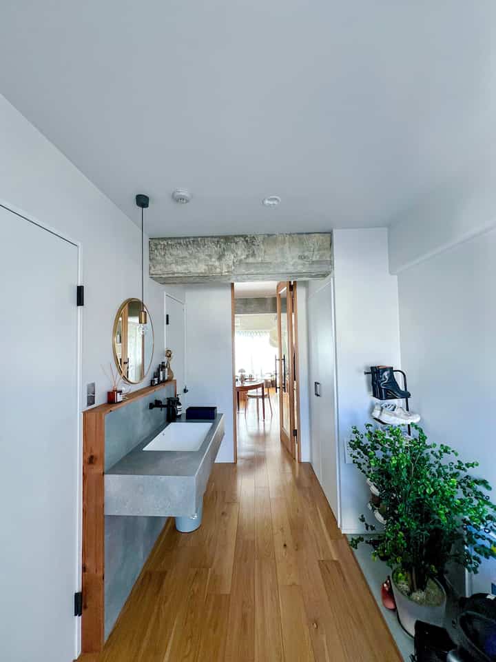 明るいホワイトと木目調の調和が取れた玄関、右側に大きな緑の植物が配置され爽やかな雰囲気のあるインテリア