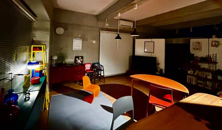 ウッドトーンとオレンジ、グレーの配色が特徴のワンルームリビング、現代的な家具とペンダントライトが配置された雰囲気のある空間