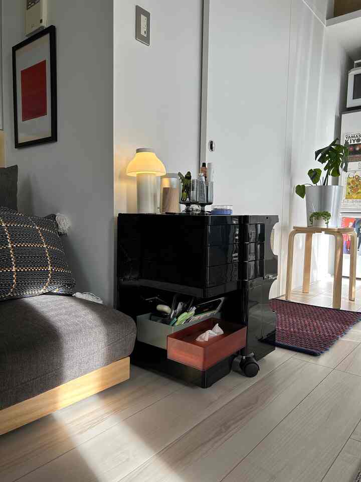 A studio apartment with white and black tones featuring a compact gray sofa and a black wheeled Boby Trolley, creating a clean and cozy interior.