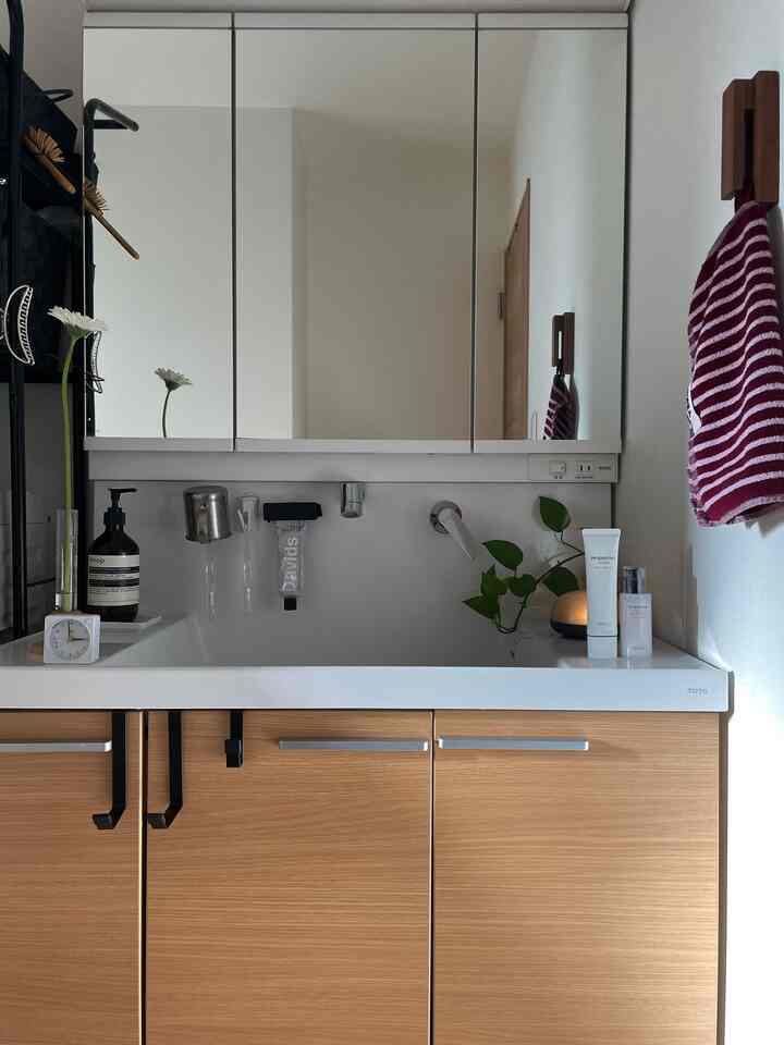 白と木目調が調和したバスルームの洗面台、整頓されたタオルと小物が配置された清潔感のある空間