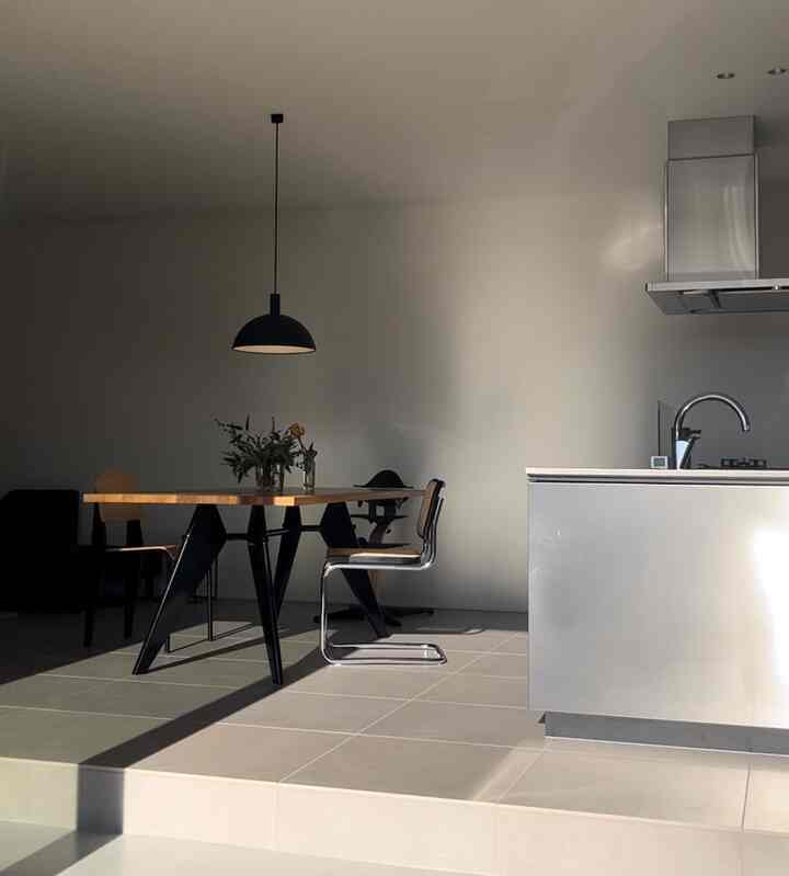 ナチュラルカラーとグレーのトーンのキッチンダイニングルーム、シンプルでモダンな家具とペンダントライトが配置された印象的な空間