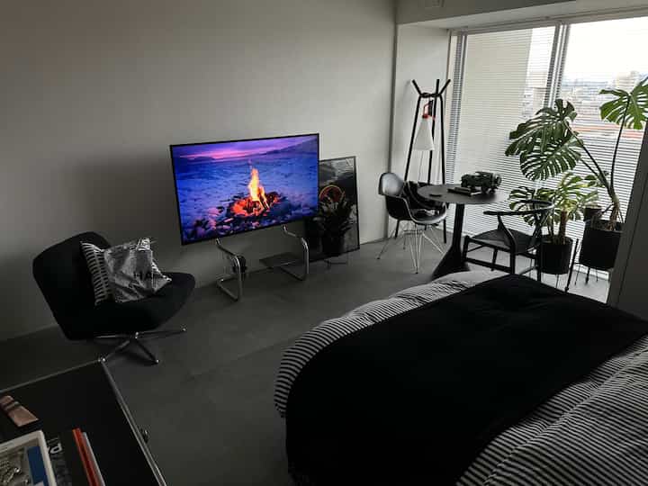 ブラックとグレーのトーンのモダンな寝室、シングルベッド、テレビ、居心地の良いアームチェアが配置された洗練されたコンパクトな空間