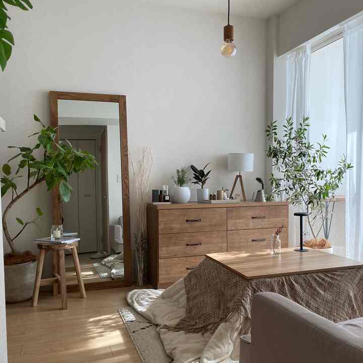 ナチュラルな木目調と白い壁のリビング、こたつテーブルと大きな鏡、観葉植物が配置された落ち着いた雰囲気のインテリア