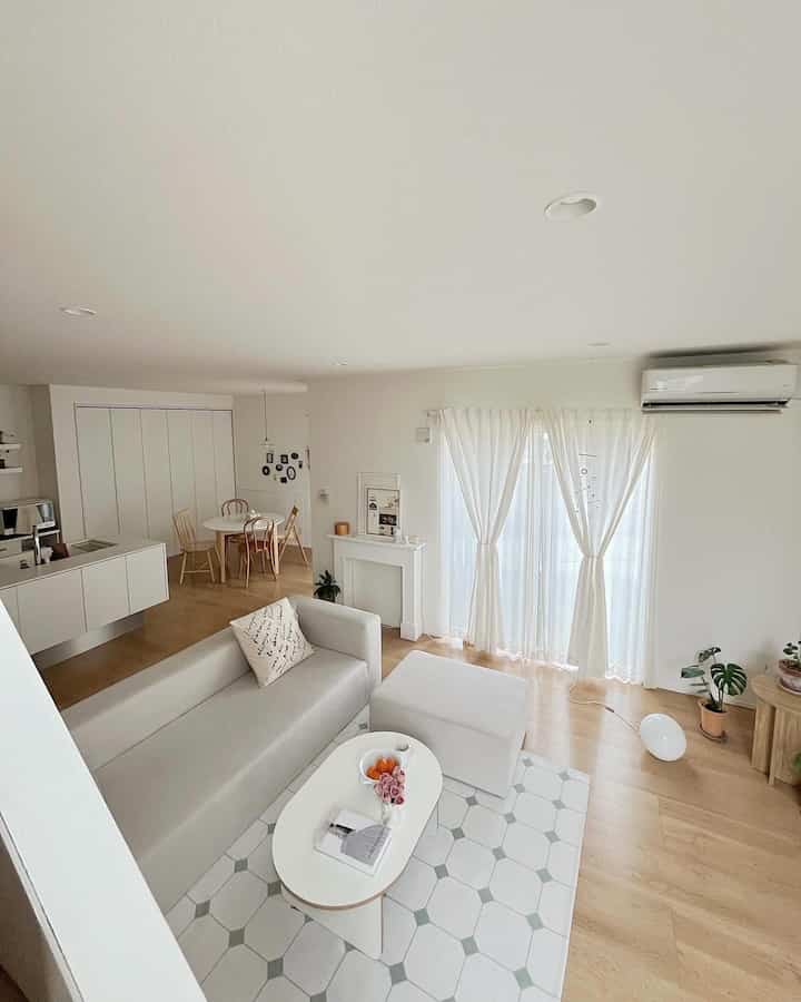 Bright white and wood tone living room featuring a sofa, curtains, and coffee table with a clean, natural ambiance