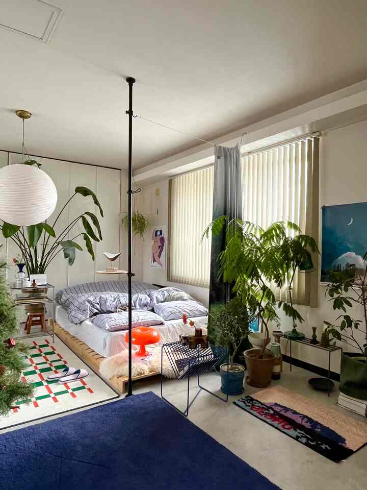 ナチュラルな色調のリビング兼寝室、木製ベッドと豊富な観葉植物が配置された雰囲気のあるインテリア