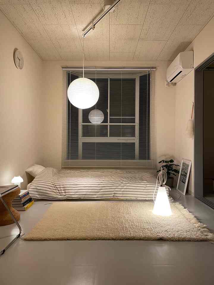 Warm beige and white-toned studio bedroom featuring a striped duvet cover and pendant light in a simple setting