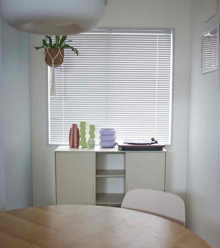 White-toned dining room featuring a white cabinet with colorful vases and a record player on top, creating a simple space
