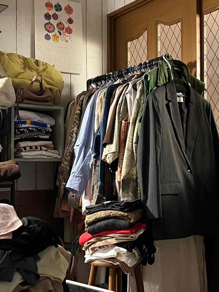 暖かい木目調とベージュ色調の狭い部屋、中央に配置されたハンガーラックと収納棚に整頓された衣類がある雰囲気のあるインテリア