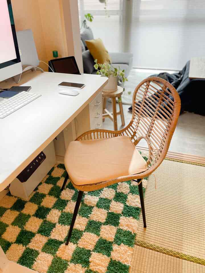 ナチュラルな色調のホームオフィス空間、白いデスクとラタンチェア、グレーのソファと緑の植物が配置された雰囲気のあるインテリア