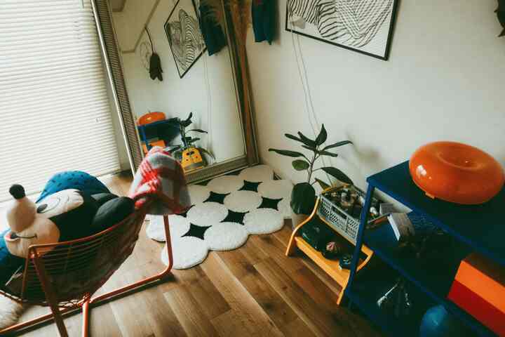 Natural color dominated studio apartment featuring a large mirror, orange sofa chair, plant, and patterned rug with cozy atmosphere