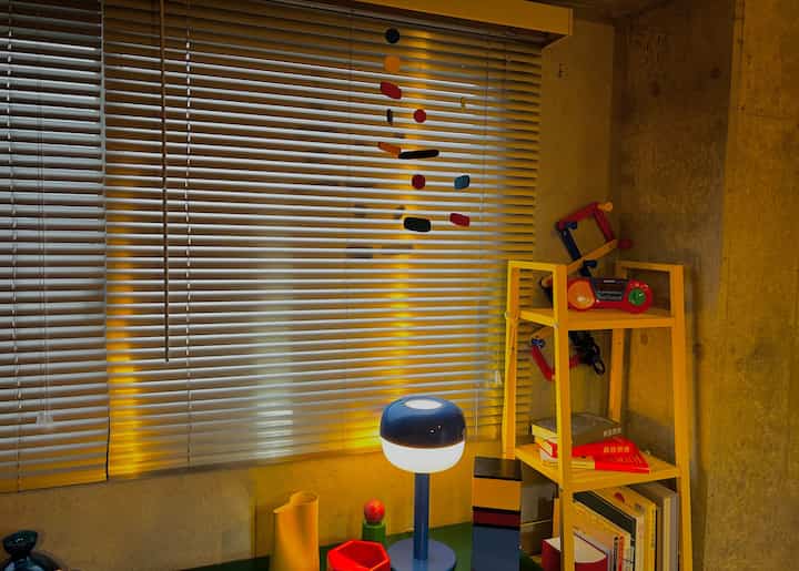 温かみのあるゴールド照明とナチュラルウッドの棚が置かれた、子供のおもちゃとモビールがある狭い部屋