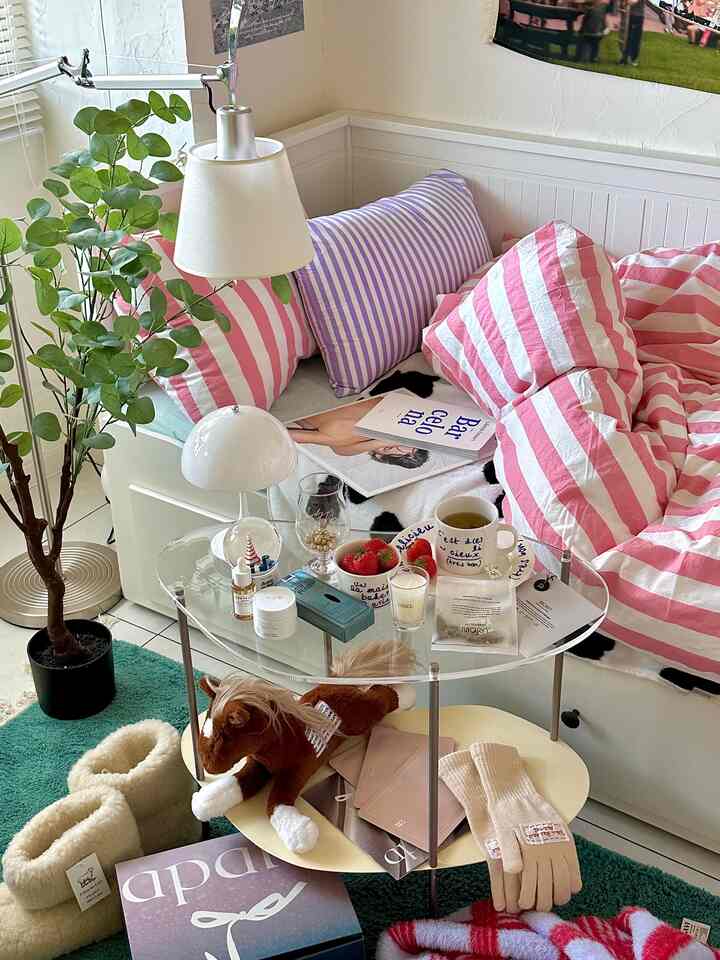 白とピンクのストライプのコーナーソファが配置されたリビングルーム、透明なアクリル製コーヒーテーブルがあり、自然でモダンな印象的な空間