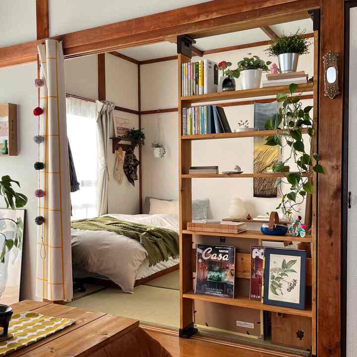 Natural wood tones and white blend in a compact studio bedroom and living area featuring bookshelf and plants creating a cozy atmosphere