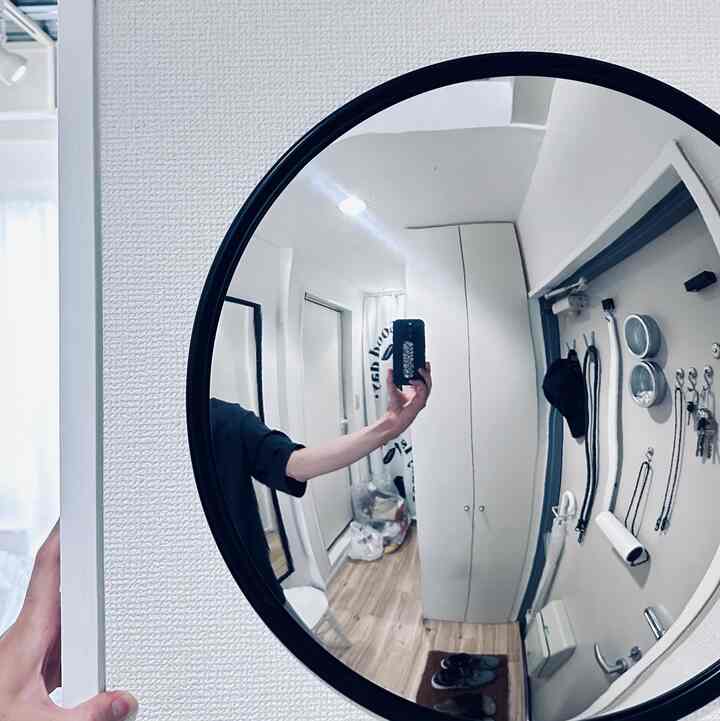 白と木目調が調和した狭いワンルームの玄関、中央に大きな円形の凸面鏡が掛けられている印象的な空間