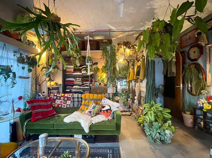 緑のソファと多くの植物が配置された昭和レトロスタイルのベランダ付きリビング