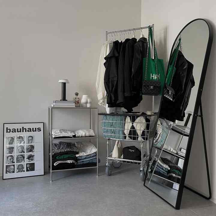 白い壁とグレーの床の空間に、スチール製の収納棚とハンガーラック、全身鏡が配置された無機質感のあるすっきりとしたインテリア