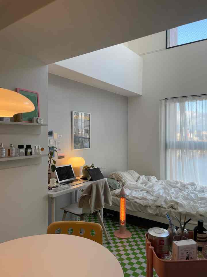 White and beige toned small bedroom featuring bed, desk, and warm lighting, creating a cozy space