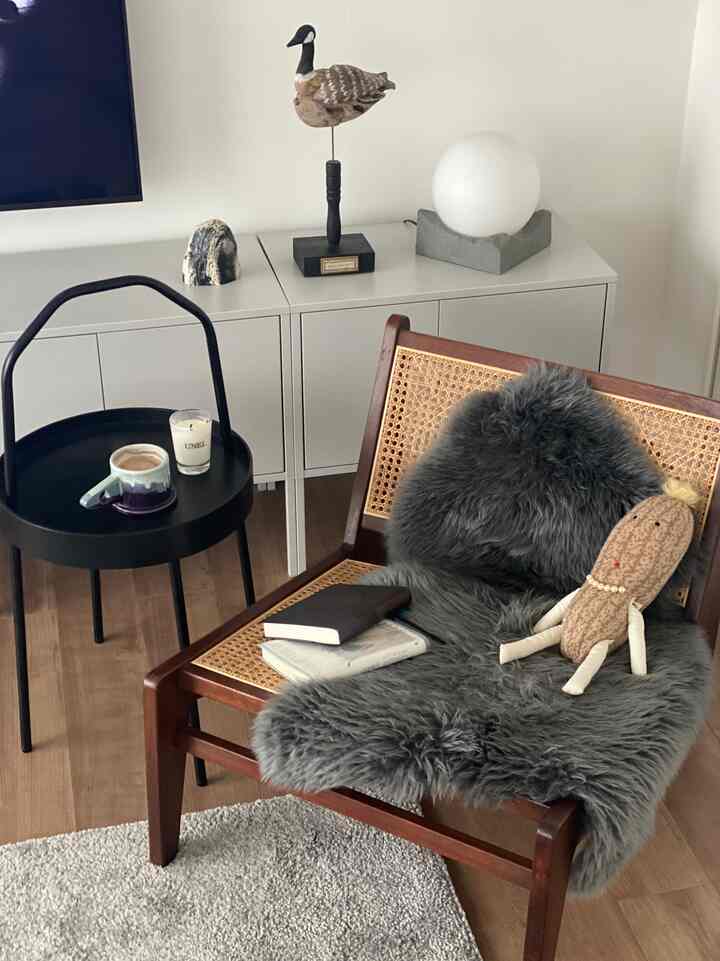 ナチュラルな色調のリビング、木製フレームのアームチェアと黒のサイドテーブル、本とキャンドルが置かれた雰囲気のある読書空間