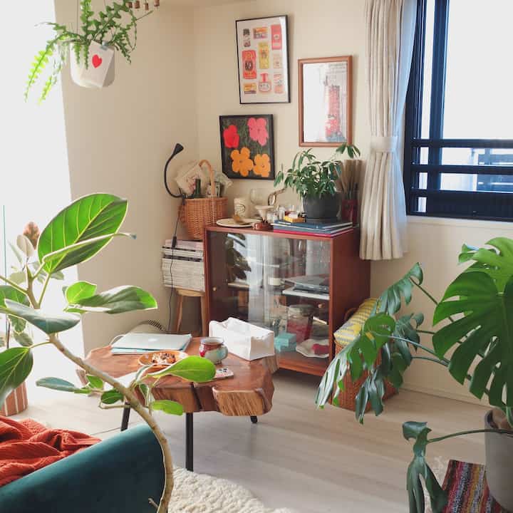 ベージュ色の壁と木目調家具を配したナチュラルスタイルのリビング、複数の観葉植物が置かれた雰囲気のある空間