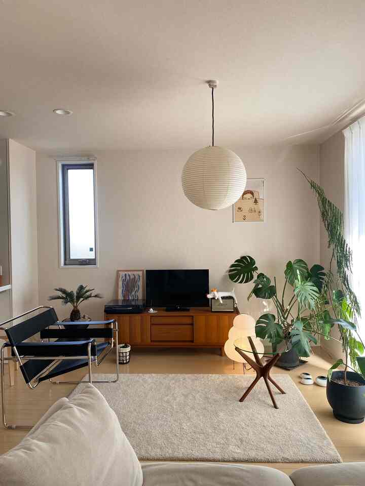 ナチュラルカラーと木目調のリビング、木製のテレビ台とペンダントライト、大型植物が配置された雰囲気のある空間