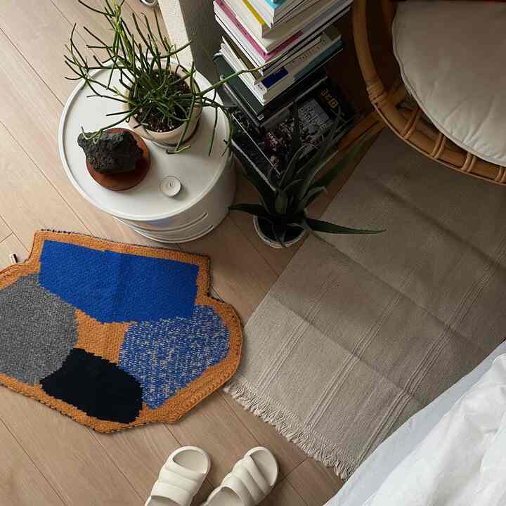 Natural wood tone flooring with beige and colorful rugs in kitchen entrance area, simple and minimal atmosphere