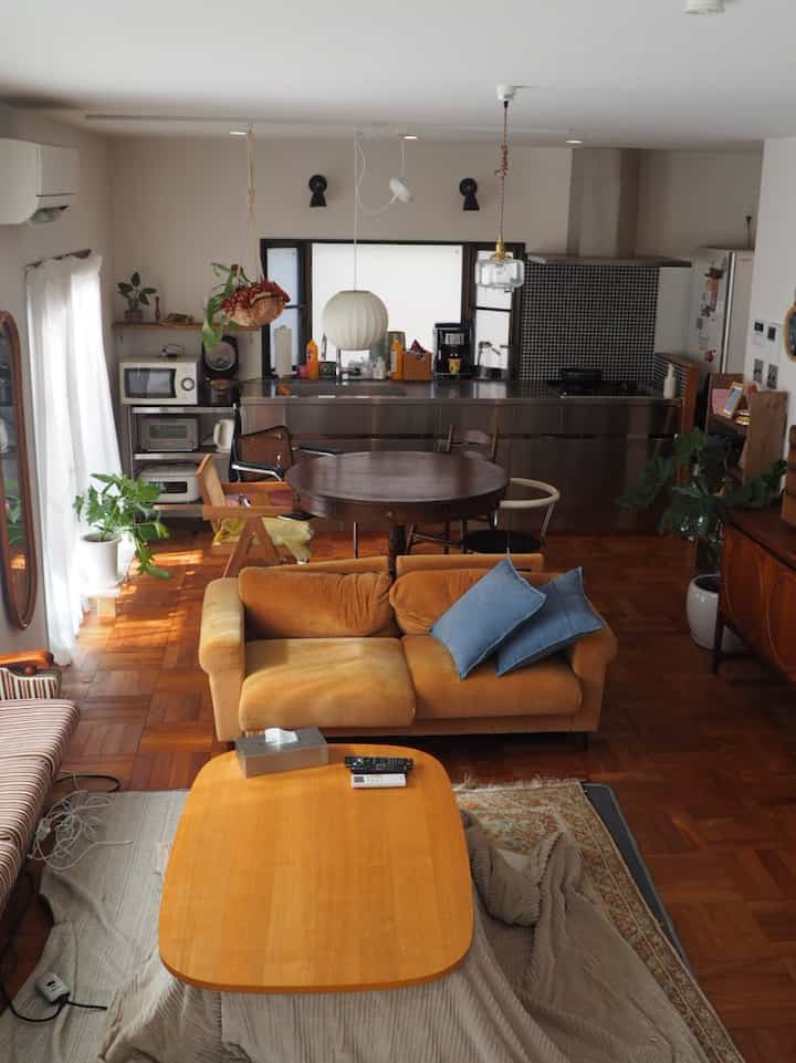 Wood tone living room and kitchen featuring an orange sofa and round dining table in mid-century modern style