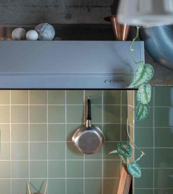グリーンタイルの壁と金属の鍋、オブジェが配されたヴィンテージ風のキッチンの一部