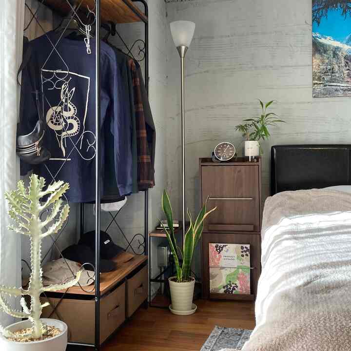 ナチュラルな木目調とグレーの壁が調和する寝室、植物とフロアランプが落ち着いた雰囲気を演出するインテリア