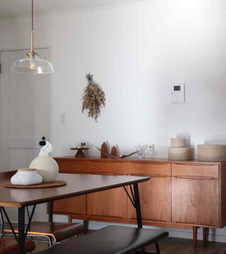 A simple and modern dining room with white walls and wood tone dining table and cabinet