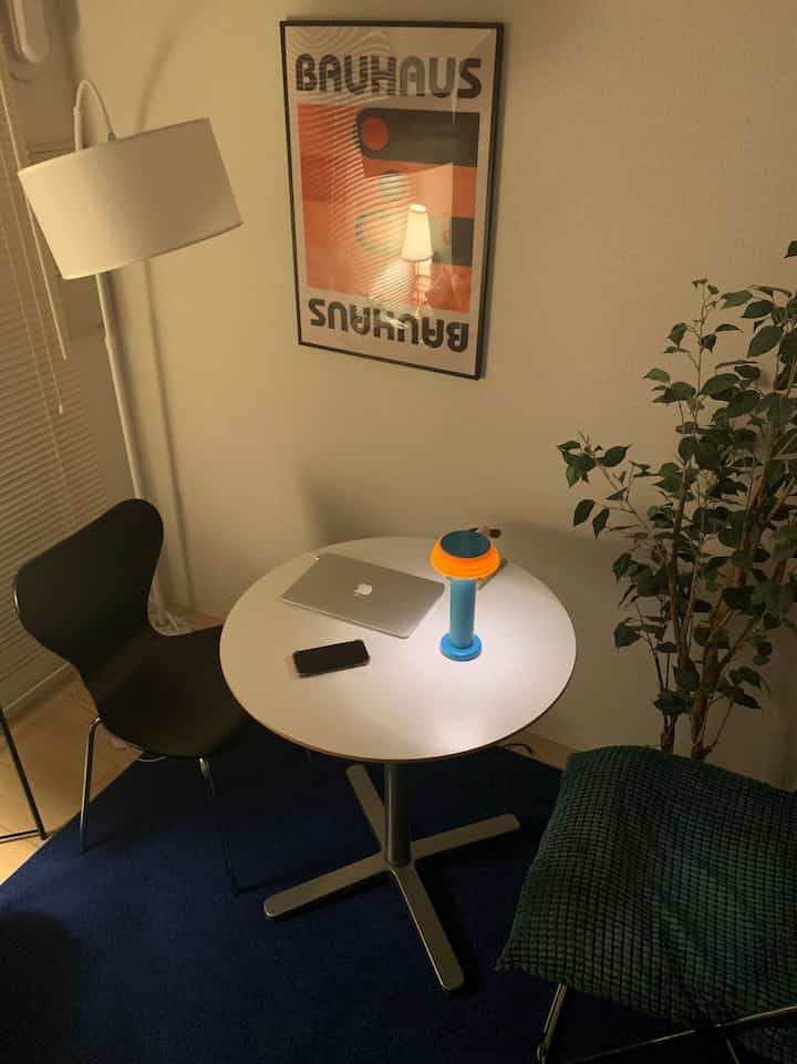 白と青の色調の6畳ワンルーム、丸いデスクとフロアランプ、植物が配置された印象的な作業空間