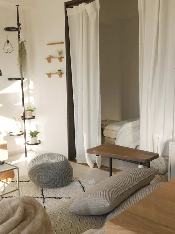 ベージュとホワイトトーンの1LDKのリビングと寝室、自然光が差し込む雰囲気のある家具配置のインテリア