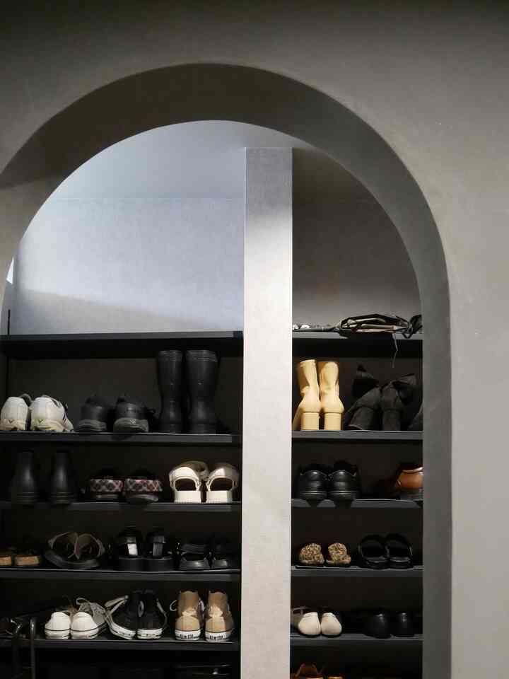 グレーと黒の色調のアーチ壁がある玄関、黒い靴棚が整然と配置された雰囲気のあるインテリア