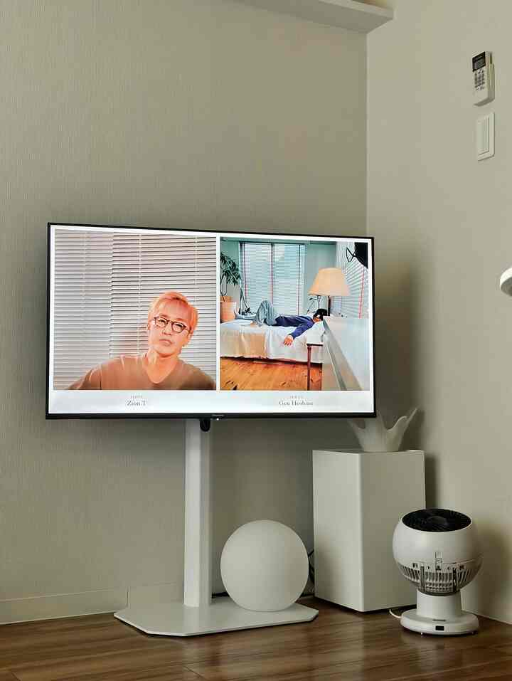 白い壁と茶色い木製フローリングが調和するコンパクトなリビング、テレビスタンドとフロアランプがモダンな雰囲気を醸し出すインテリア