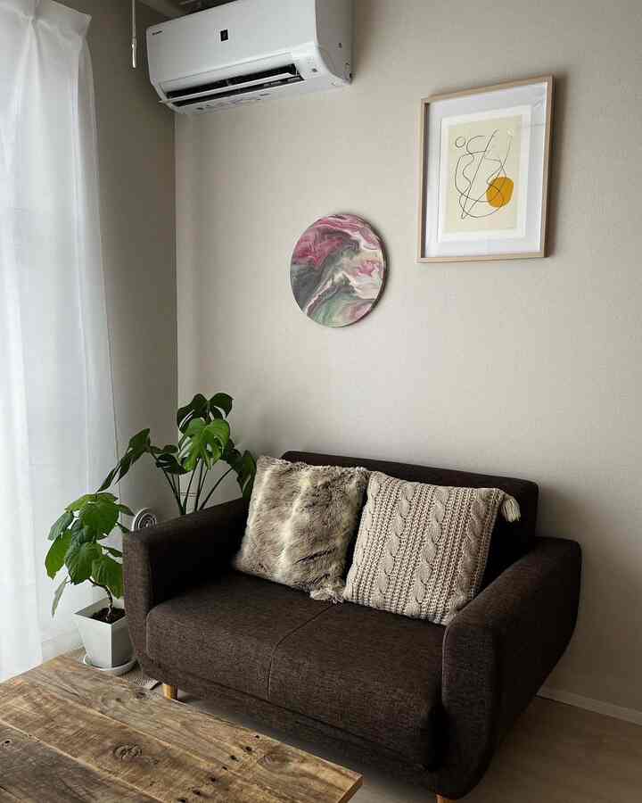 ベージュの壁とダークブラウンの二人掛けソファ、木製テーブルと植物が配置された落ち着いたリビング