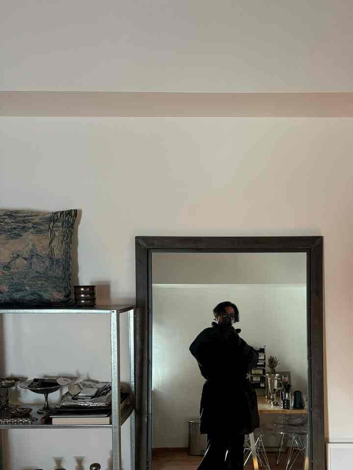 白い壁と茶色の床が調和する一人暮らし用ダイニング、モダンな空間に大きな鏡と金属製の棚が配置されている