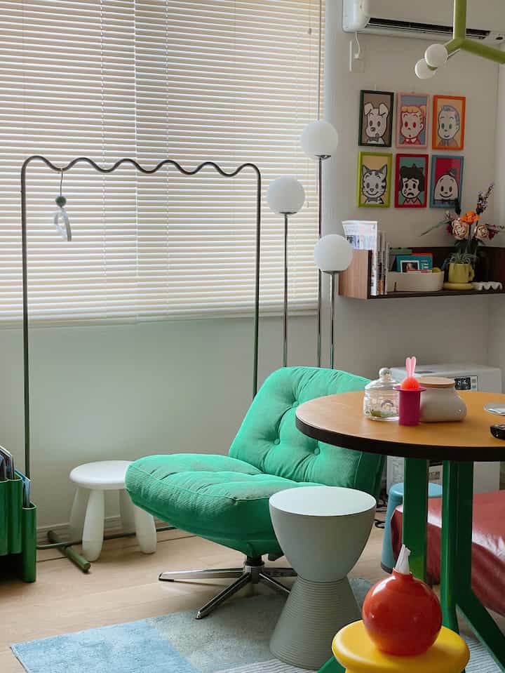 Bright living room with a green armchair and orange round table in front of white blinds