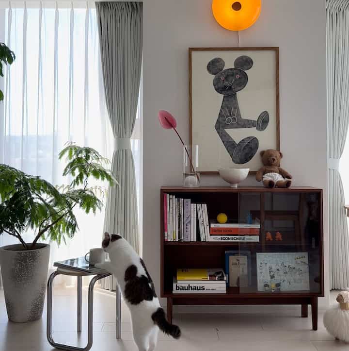 明るく白を基調としたリビング、中央にブラウンの棚と観葉植物、猫が小さなテーブルに乗った雰囲気のある空間