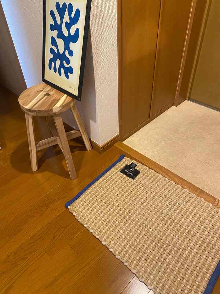 Entrance area with wood tones and blue accents, featuring a wooden stool and a HAY door mat in a neat setting