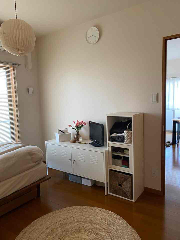 Bedroom with white walls and wood tone floor, featuring bed frame and cabinet in a simple natural setting