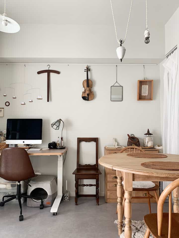 A white-walled space with natural brown wood furniture, featuring a computer desk and round dining table, creating a harmonious workspace and dining area for two