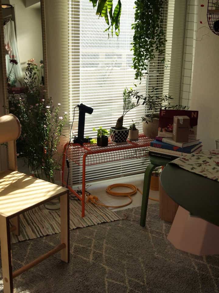 暖かな陽射しが差し込む窓辺に植物とオレンジのスツールが置かれたナチュラルなバルコニーのインテリア