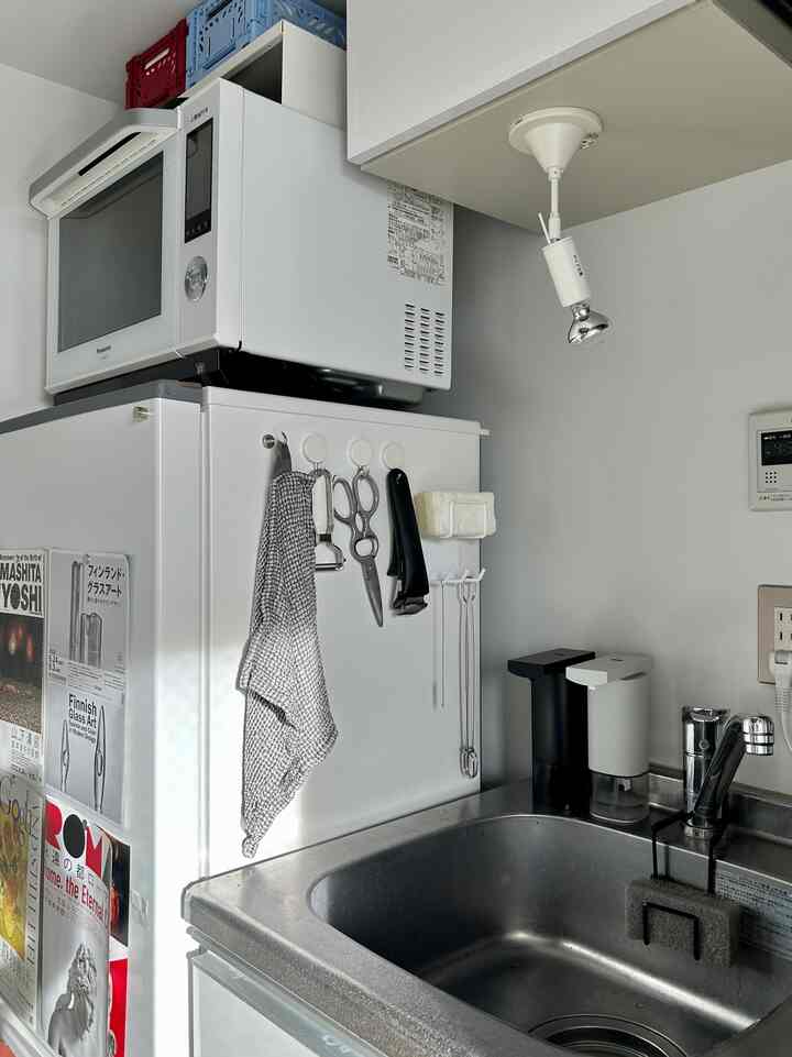 白とグレーの色調のコンパクトなキッチン、冷蔵庫上の電子レンジとシンク、整然と配置された調理器具がある雰囲気のあるインテリア