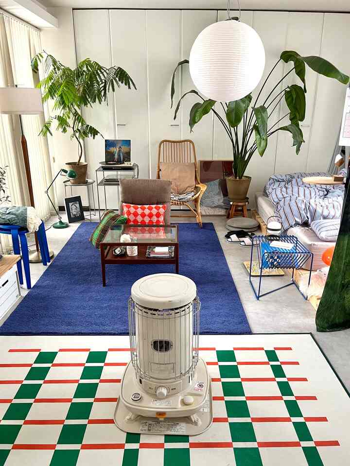 Navy and green toned living room with bedroom area, featuring wooden chair and rugs creating a cozy, warm atmosphere