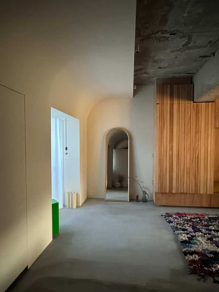 ホワイトとウッドトーンの玄関、アールデコ風のアーチ天井と大きなアーチ型の鏡、コンクリート床が調和したミニマルな空間