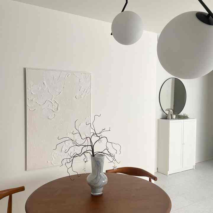 白と茶色の色調のリビング、丸いダイニングテーブルと木製の椅子、鏡が配置された自然でシンプルな印象的な空間