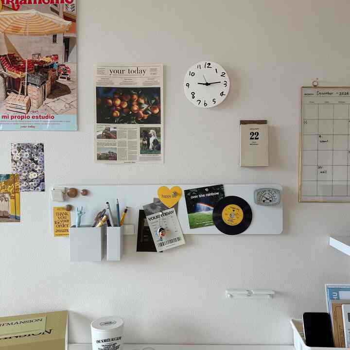明るい白い壁にシンプルな机、時計や壁の装飾が配置された、清潔で開放感のあるワークスペース