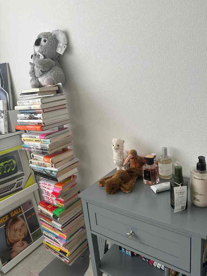 白い壁とグレーのサイドテーブル、本棚、ペットのぬいぐるみが配置された落ち着いた書斎空間
