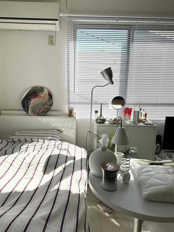Bright white and silver-toned bedroom featuring striped duvet cover, floor lamp, and a modern, clean atmosphere